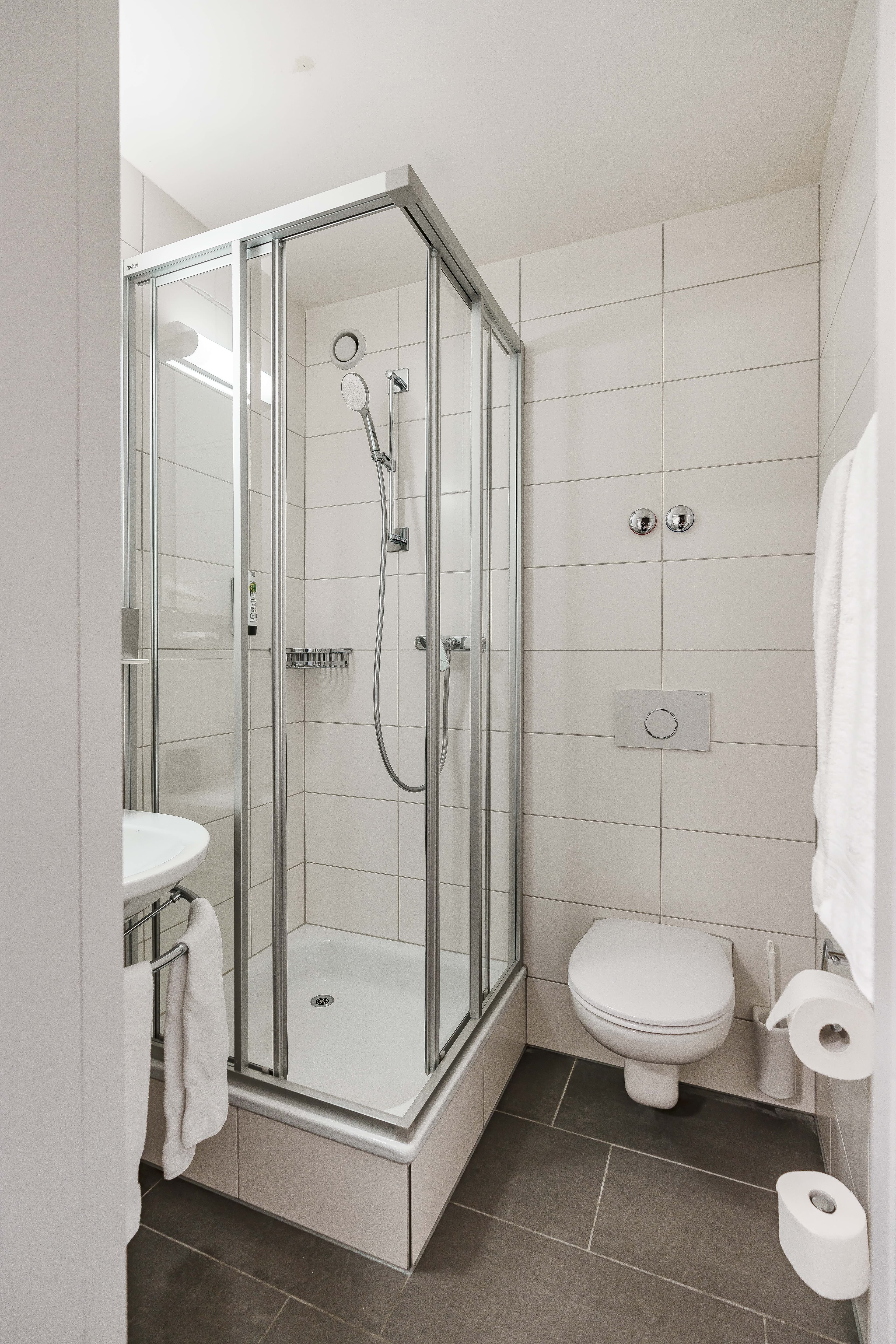 A simple bathroom in a single room at the Flex Motel Wil with a glass enclosed shower a toilet and a sink