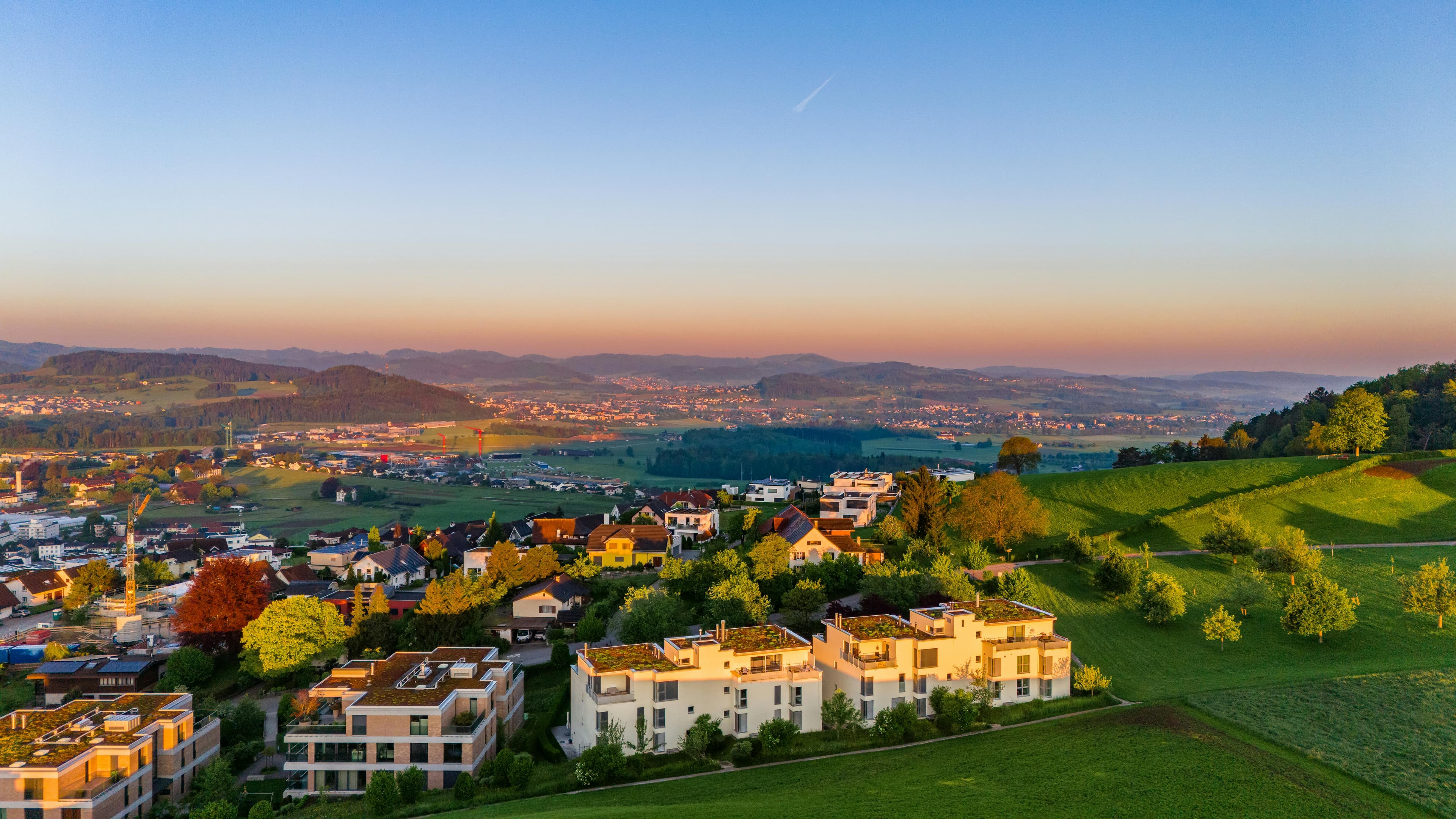 Aerial view of a picturesque landscape around Wil with modern houses in the foreground and a wide view over fields and hills in the background under a clear sky.