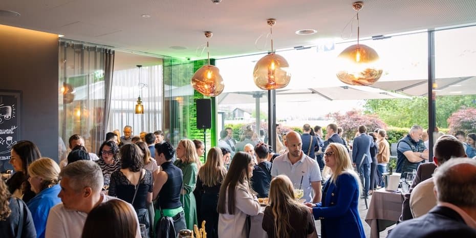 A lively event with many people is taking place in a modern, well-lit indoor space with large windows.