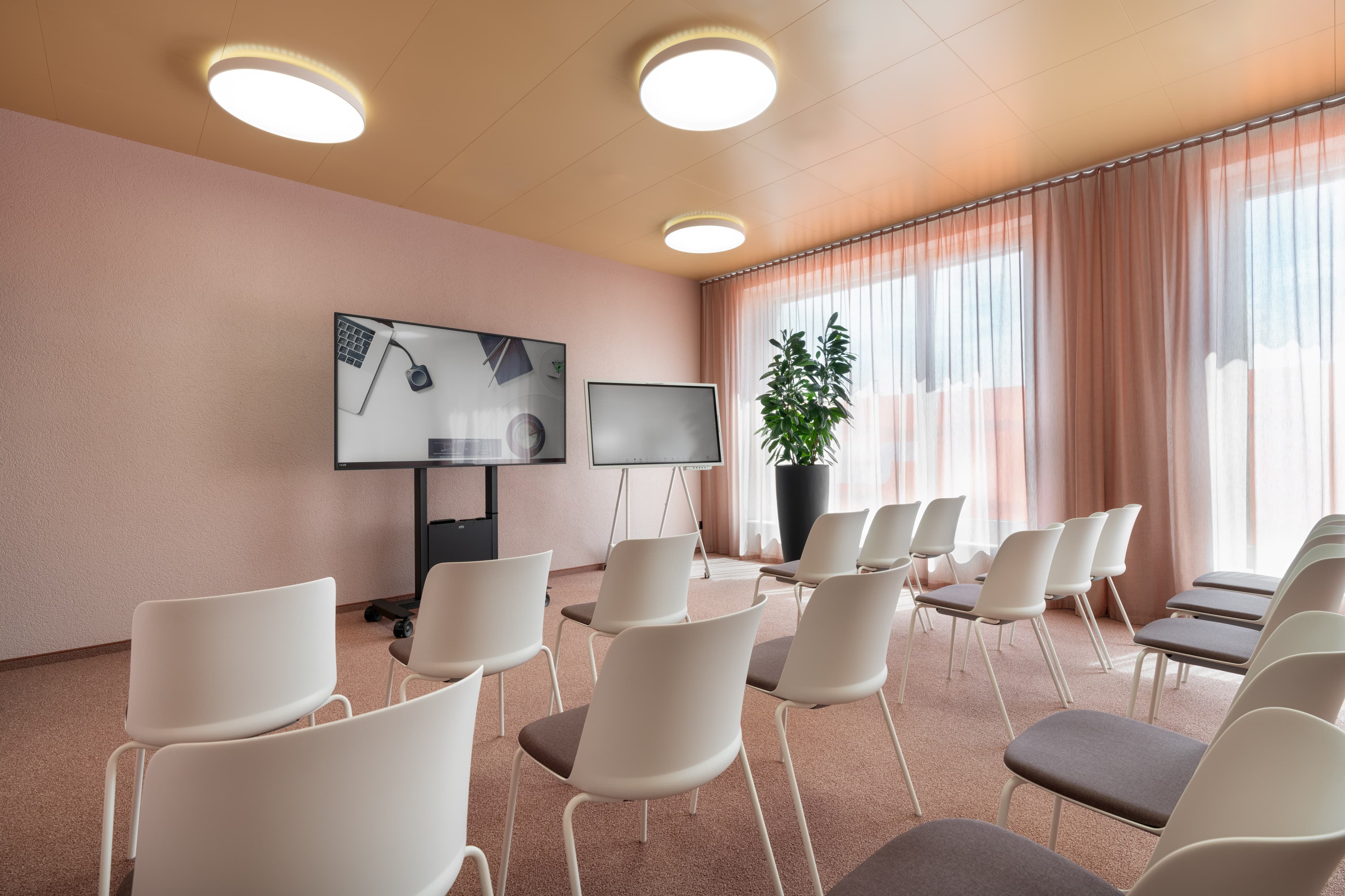 A modern conference room in the b_smart hotel Arbon with white chairs a large screen and a flip chart