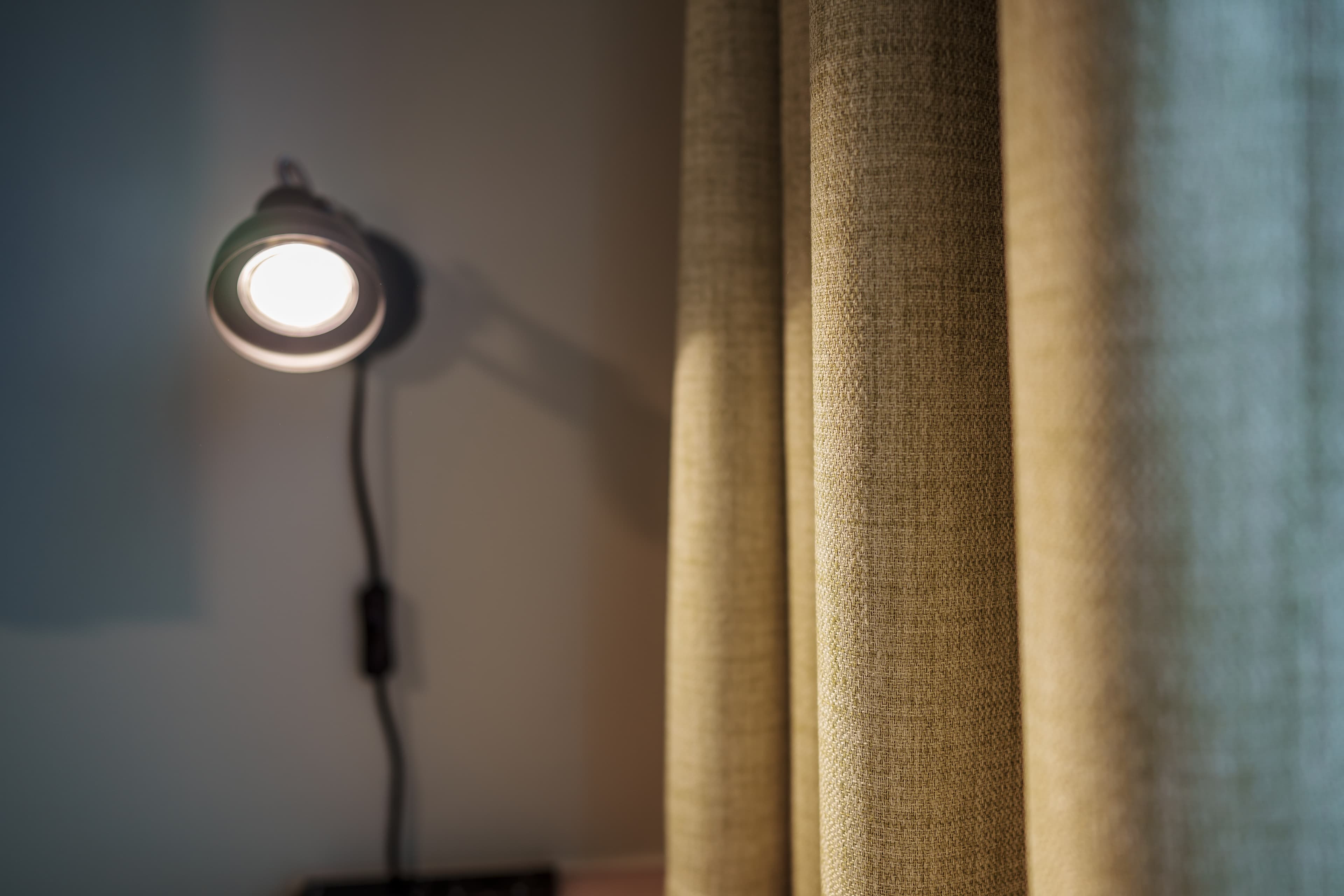 A wall lamp shines next to a beige curtain in a single room at the Flex Motel Wil.