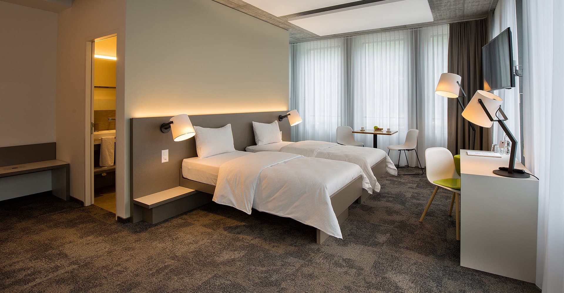 Junior suite at B Smart Motel Landquart with two twin beds, modern desk, and a TV on the wall