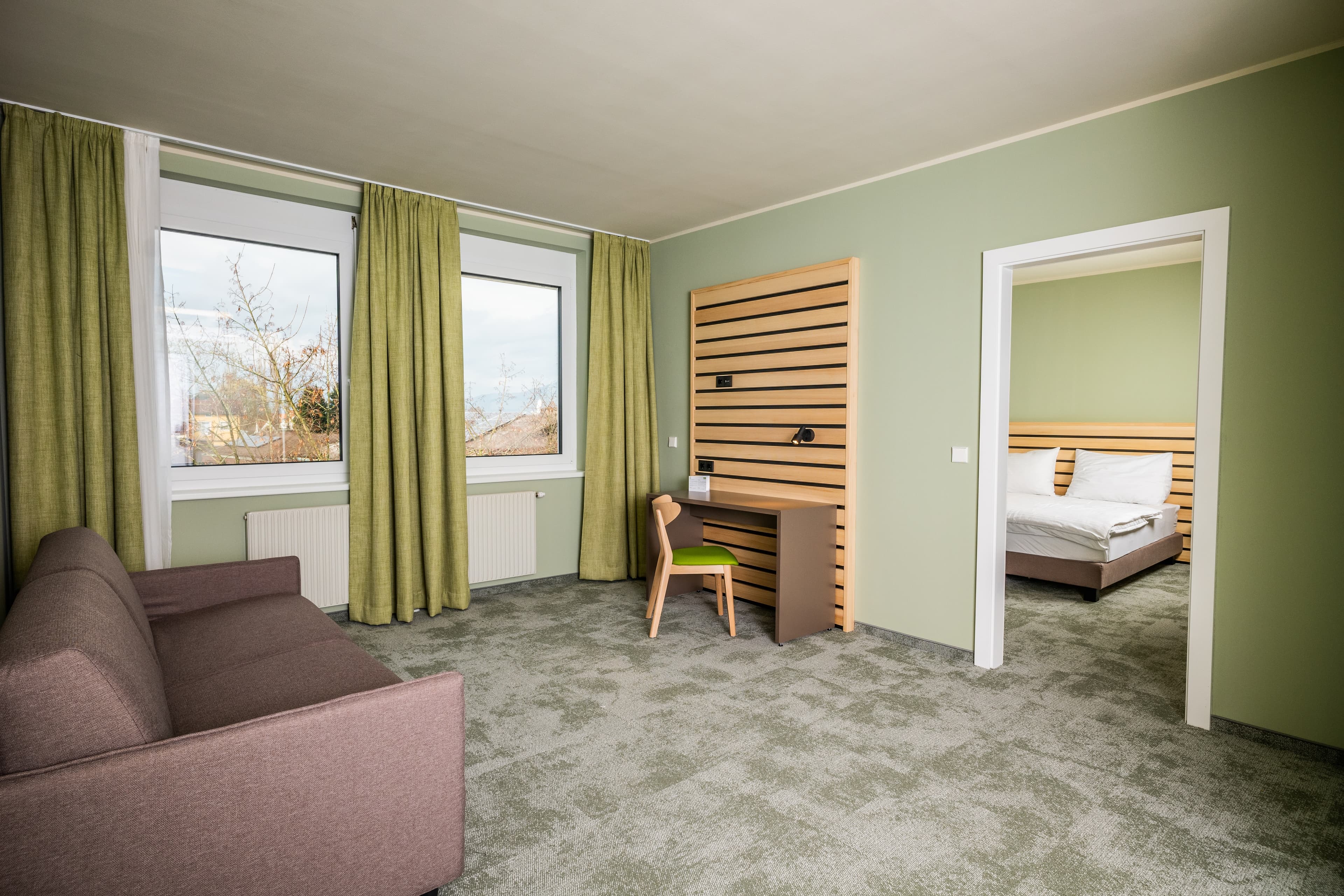 A modern hotel room in the Junior Suite Standard at the Flex Motel Spielberg with a sofa a desk and an adjoining bedroom
