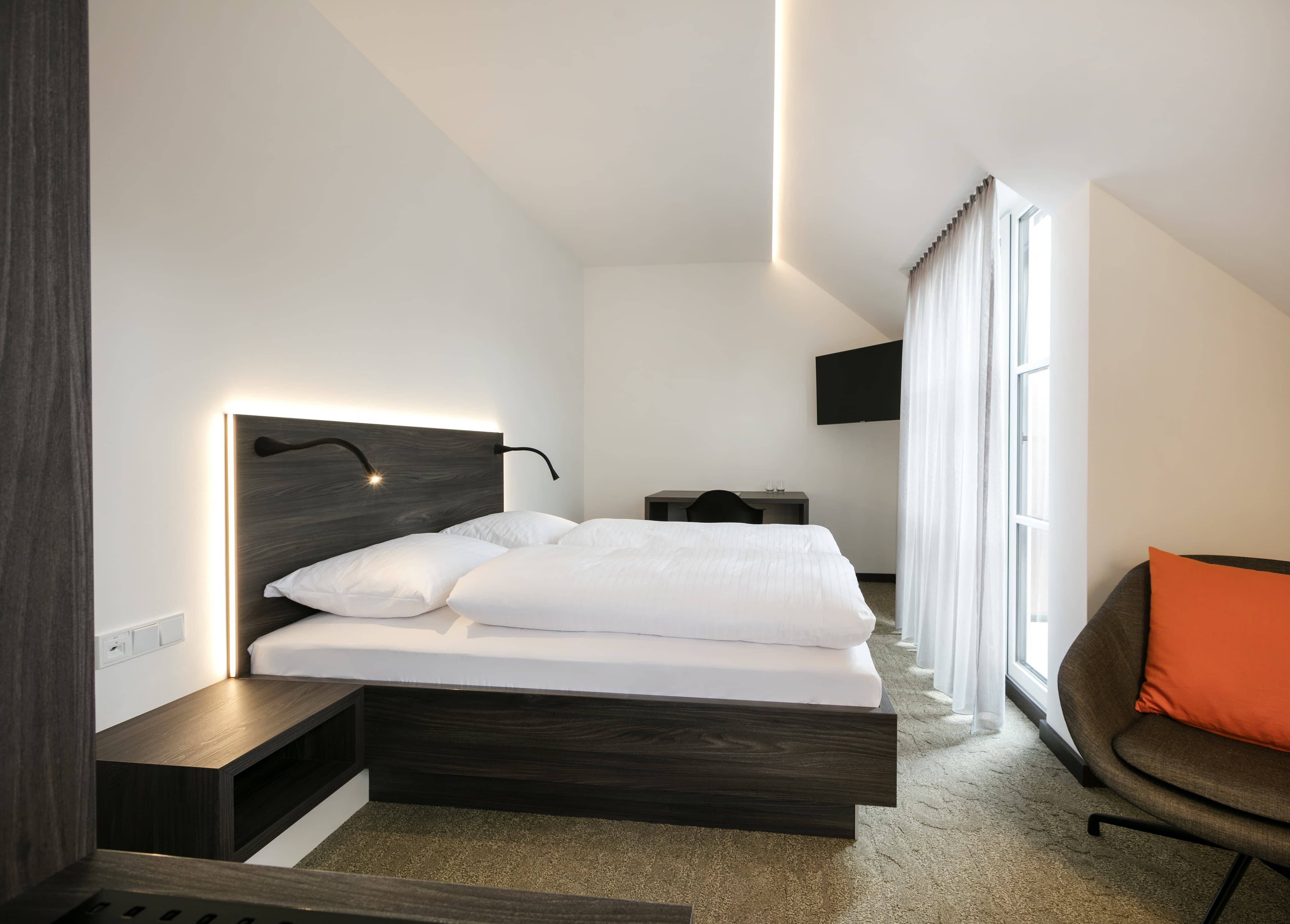 A modern double room in the Spitzerberg Hotel with a large bed, a desk, and an armchair with an orange cushion