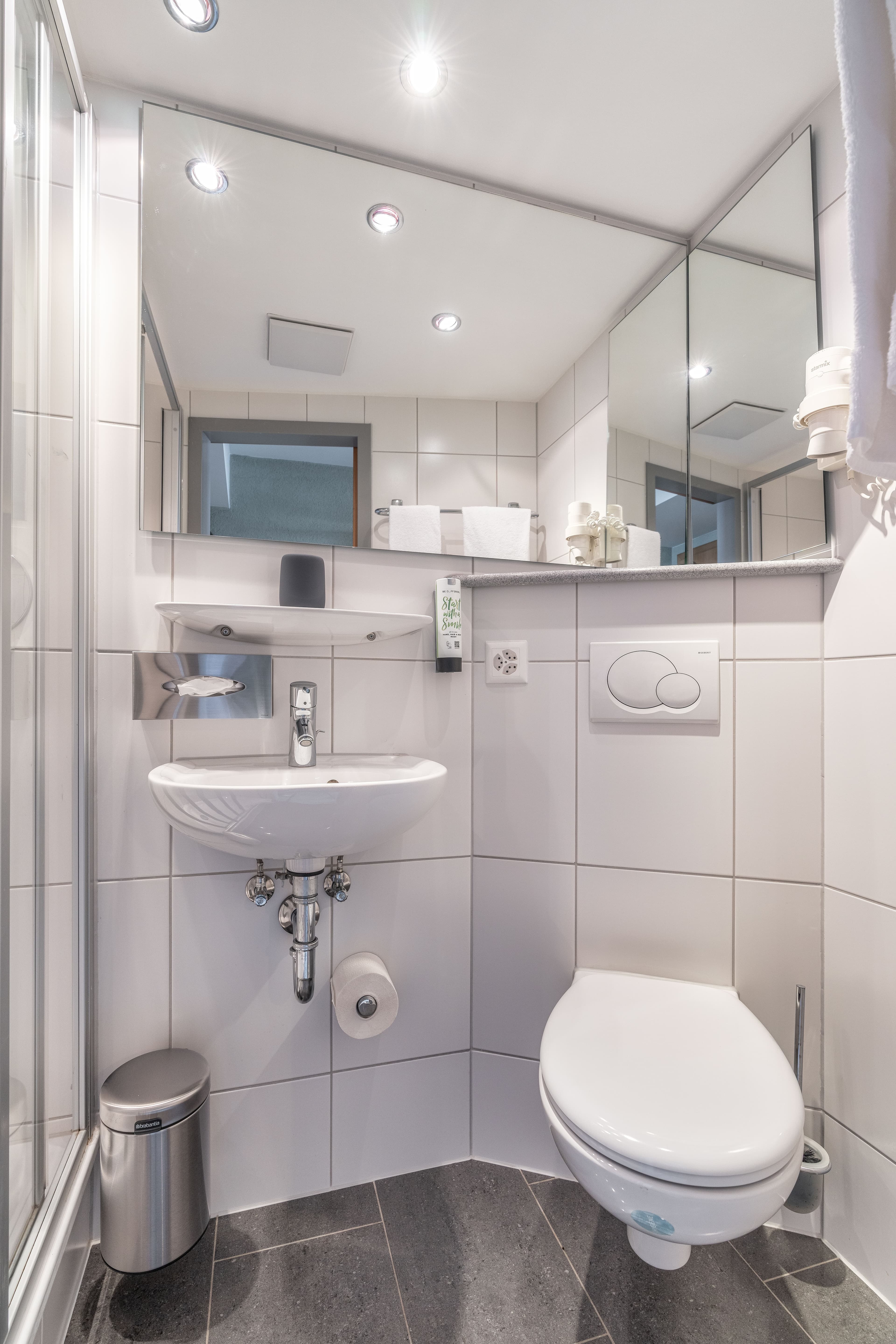 A modern bright bathroom in the Flex Motel Schonenwerd with a sink toilet mirror and shower.