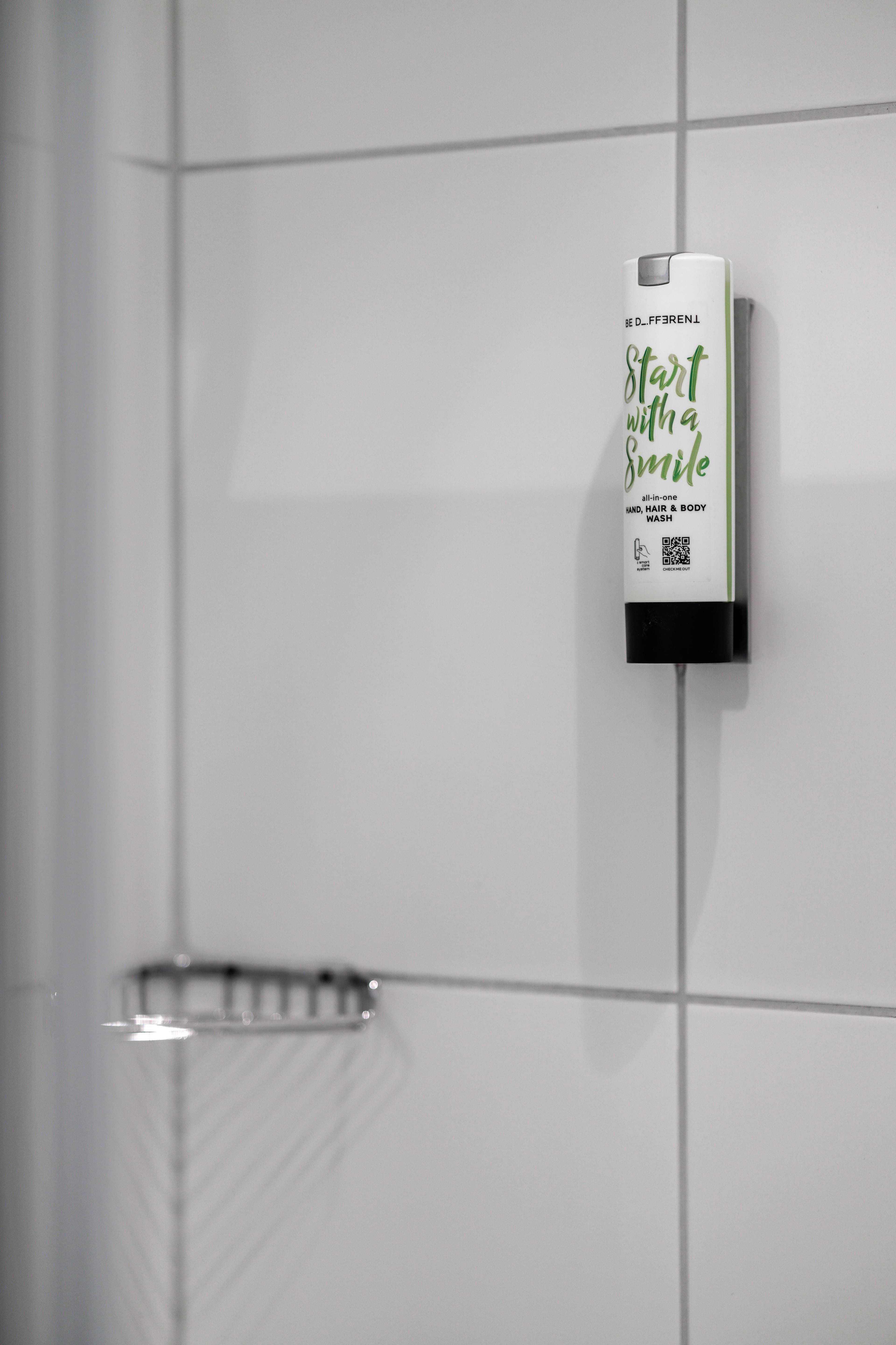 A bottle of shampoo labeled Start with a Smile hangs on a white bathroom wall.
