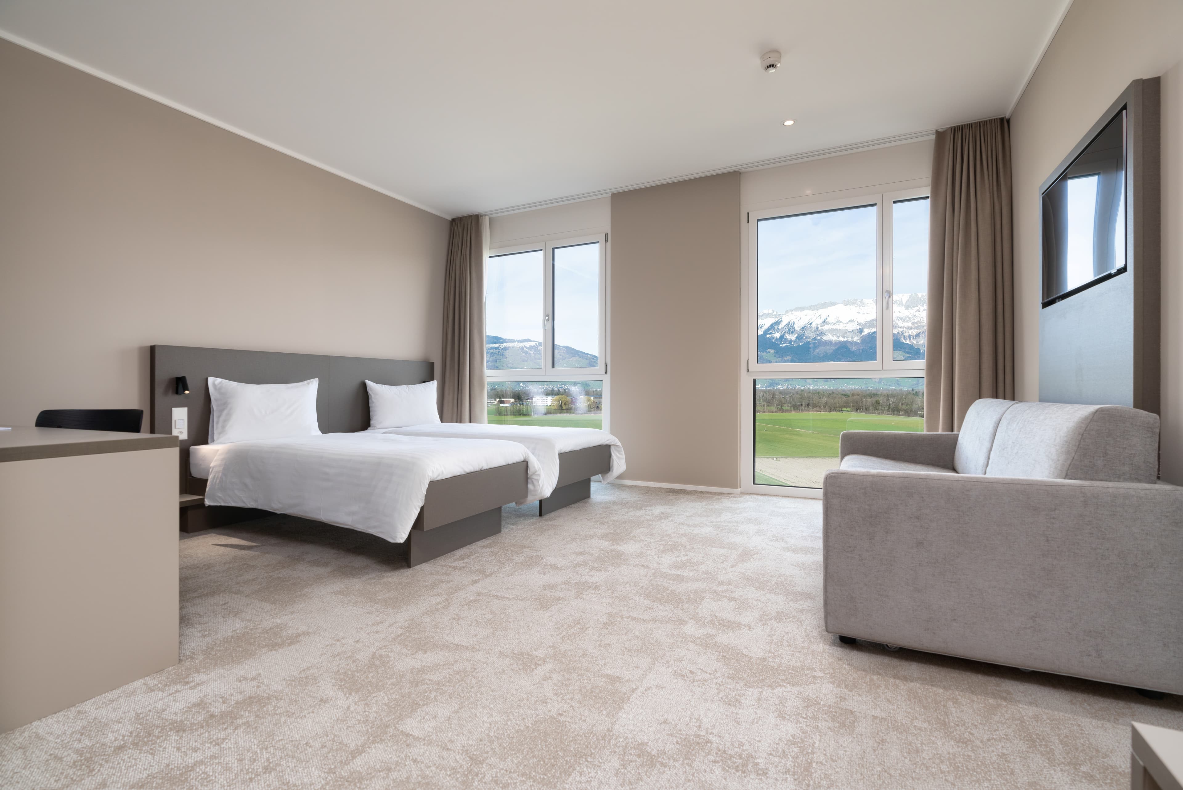 Spacious Junior Suite in the B_Smart Motel Schaan with two beds, a sofa, large windows, and mountain views.