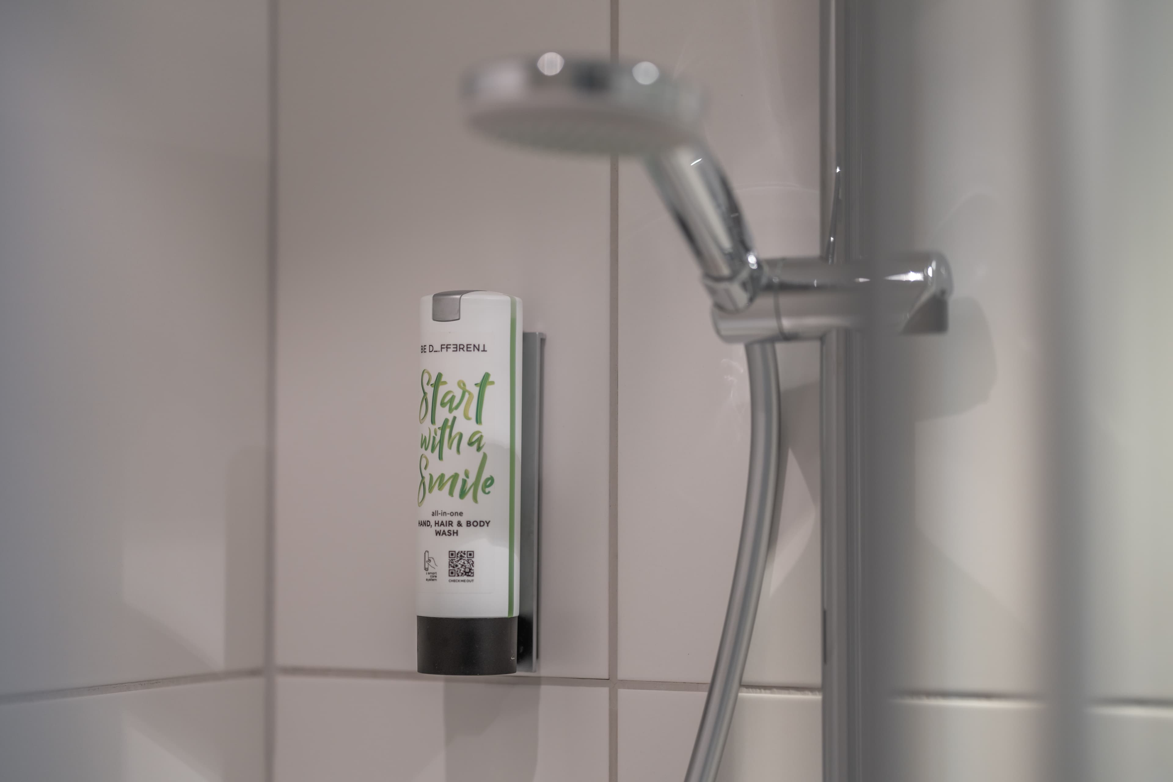 A dispenser labeled Start with a Smile hangs on the tiled shower wall in the Flex Motel Schonenwerd.