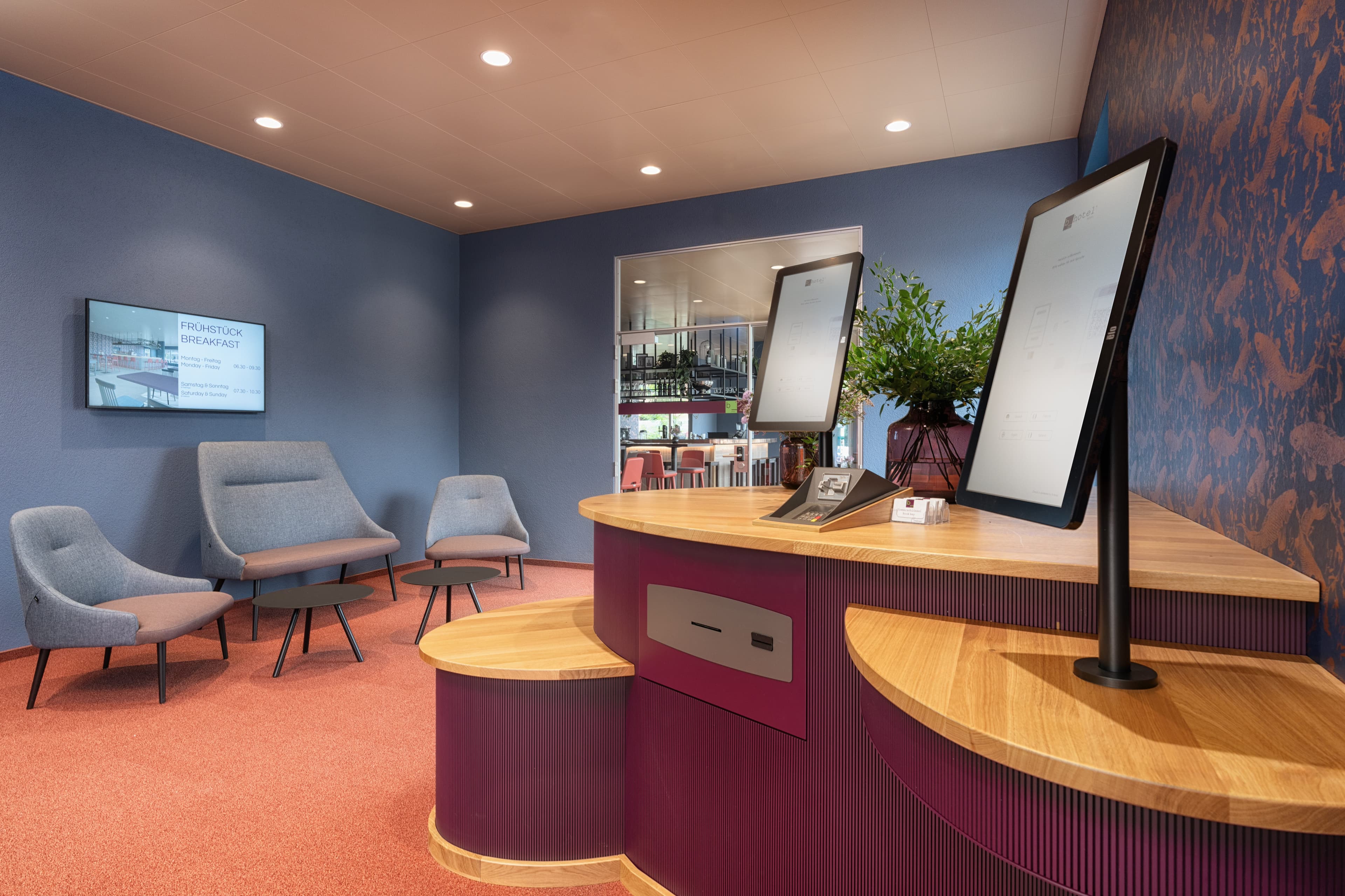 A modern self-check-in area at the B Smart Hotel Arbon with blue walls seating and a digital terminal on a wooden counter