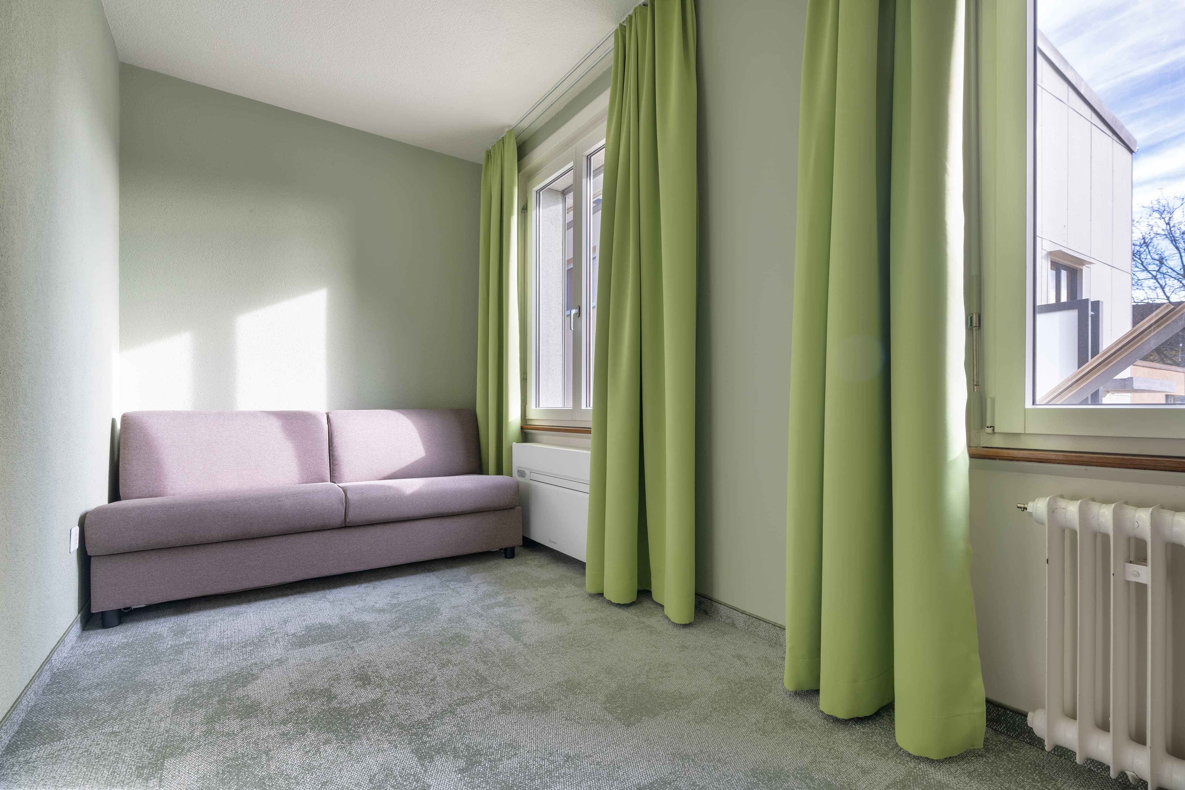 A simply furnished room in a hotel in Schonenwerd with a purple couch green curtains and a window with a view